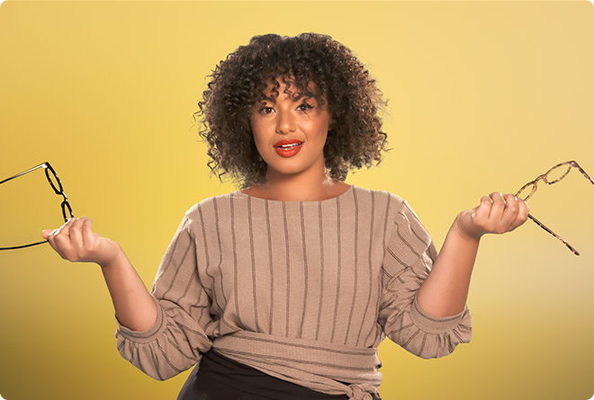 Female model poses confidently for the camera while holding two pairs of glasses against yellow background