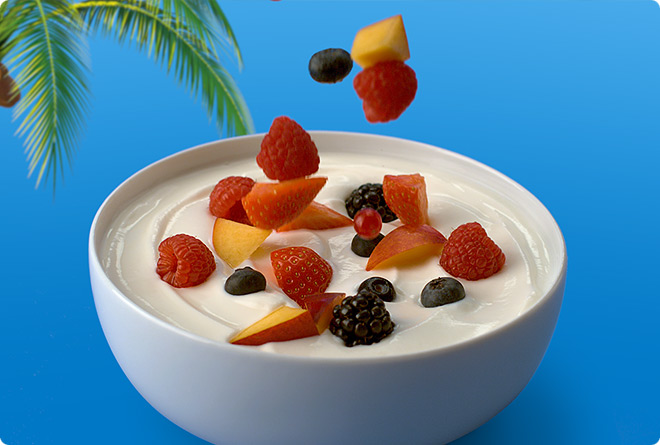 A bowl of Koko yogurt with fresh breakfast fruits and berries cascading into it