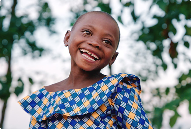 A smiling girl wearing a bright dress looking happy after undergoing a cleft palate surgery from the Operation Smile medical team