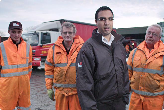 Four workers in orange all-weather branded workwear standing infront of a fuel delivery lorry
